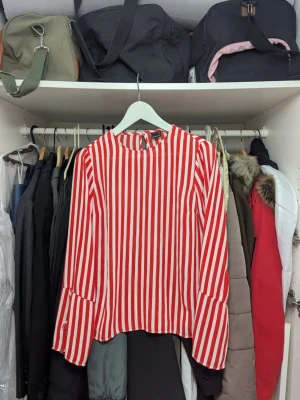 Röd- och vitrandig blus Gina Tricot - Snygg blus från Gina Tricot med röda och vita vertikala ränder. Blusen har lång ärm med knappdetalj vid ärmslut och en rak passform. Tillverkad i ett lätt och mjukt tyg som ger en skön känsla. Perfekt för att lyfta din outfit med lite färg.