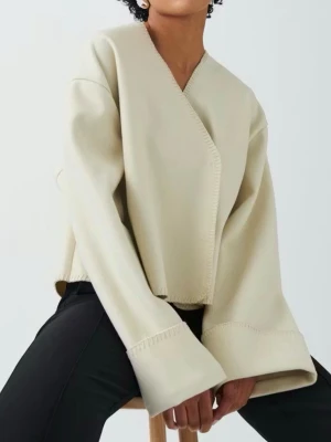 Vit jacka  - Trendig beige kofta med oversized passform och vida ärmar. Koftan har en snygg omlott-design och dekorativa sömmar längs kanterna. Perfekt för dig som gillar en minimalistisk och modern stil. Materialet ser ut att vara mjukt och lite tjockare för extra komfort.