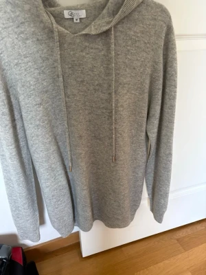 Ljusgrå hoodie från Garde Grisch - Mysig ljusgrå hoodie från Garde Grisch i mjukt material. Klassisk modell med huva och dragsnören, samt långa ärmar. Perfekt för chill dagar eller när du vill ha en enkel och stilren look.