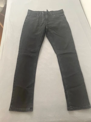 Svarta raka jeans - Svarta jeans med rak passform och klassisk femficksdesign. Jeansen har synliga sömmar och dragkedjegylf. Perfekta för en stilren och enkel look. Materialet är denim.