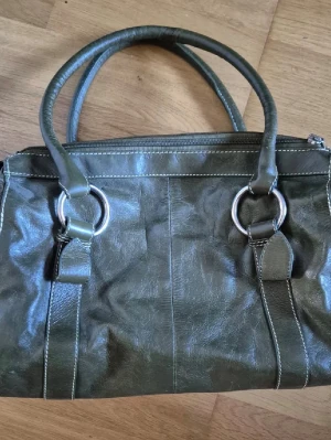 Olivgrön handväska  - Snygg olivgrön handväska i glansigt konstläder. Använd ett fåtal gånger. Pruta på!