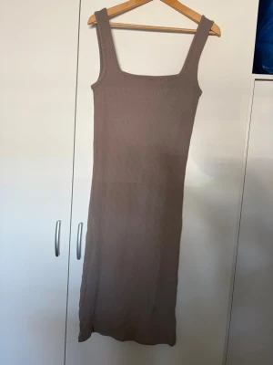 Beige ribbad långklänning 157 - Säljer en beige ribbad långklänning från 157 med breda axelband och fyrkantig ringning. Klänningen är figurnära och har en enkel, stilren design som passar perfekt till sommaren. Materialet är mjukt och stretchigt för en bekväm passform.