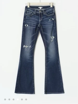 Blå bootcut jeans med slitningar - Snygga blå bootcut jeans med slitna detaljer och hål på benen. Jeansen har klassisk femficksdesign, markerade sömmar och låg midja. Perfekta för en avslappnad och trendig look. Xs 14+