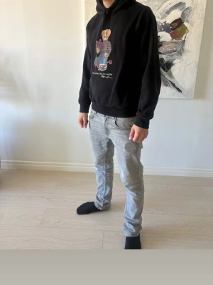 Svart hoodie Polo Ralph Lauren - Säljer en svart hoodie från Polo Ralph Lauren med den klassiska björnen på bröstet. Hoodien har huva med dragsko och ribbade muddar vid ärmar och midja. Perfekt för dig som gillar streetwear och vill ha något bekvämt och stilrent.