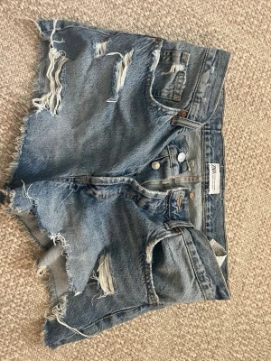 Blå slitna jeansshorts från Zara - Säljer mina blåa jeans shorts från Zara med slitningar🌸 Shortsen är köpta med slitningar så de ska vara så som de är💗 Shortsen är 40 men skulle ändå säga att de passse 38 också!!