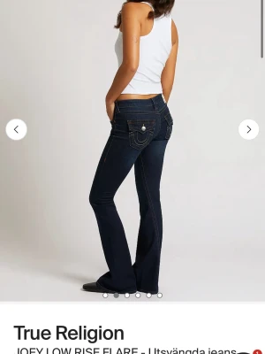 True Religion utsvängda jeans - Mörkblå utsvängda jeans från True Religion med låg midja och klassiska kontrastsömmar. Bakfickorna har dekorativa detaljer och knappstängning. Perfekta för dig som gillar en retroinspirerad look med snygg passform.
