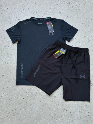 Svart träningsset från Under Armour - Snyggt svart träningsset från Under Armour med t-shirt och shorts. T-shirten har rund hals och tryckt logga på bröstet samt texten UNDER ARMOUR på sidan. Shortsen har elastisk midja med dragsko, logga på benet och texten ARMOUR. Perfekt för gym eller löpning.