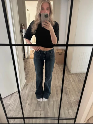 Mörkblå bootcut jeans med fickor - Säljer ett par mörkblå bootcut jeans med midwaist midja och stora framfickor. Jeansen har en klassisk femficksdesign och stängs med knapp och dragkedja. Perfekta för en avslappnad och trendig look. Köpte för 1 månad sen för 700 kr och använt 1 gång. Storlek 34