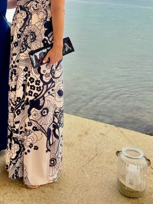 Byxdress / långklänning från Ted Baker - Säljer en elegant vit långklänning som är en byxdress med stora marinblå blommor och grafiska detaljer. Klänningen har figurnära passform upptill och faller snyggt längs kroppen. Kan passa både M och L. Perfekt för sommarens tillställningar!