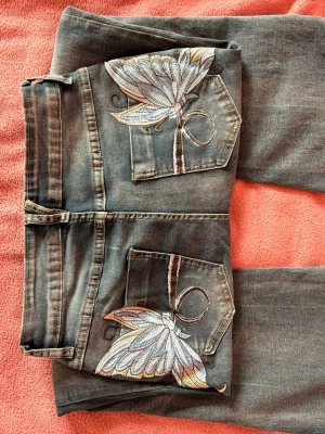 Blå jeans med broderade fjärilar - Säljer ett par blå jeans med utsvängda ben och snygga broderade fjärilar på bakfickorna. Aldrig använda 