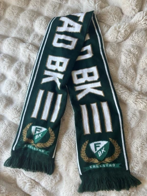 Färjestad BK halsduk grön-vit - Supporterhalsduk för Färjestad BK i grön och vit med klubbens logga och texten 'Färjestad BK Karlstad'. Halsduken har fransar i ändarna och är perfekt för att visa ditt stöd på matchen. Tillverkad i mjukt, stickat material. Andvänd 1 gång. Nypris 300+kr