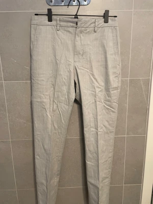 Ljusgrå kostymbyxor Tommy Hilfiger - Ser lite skrinkliga ut men det är för de har legat i garderoben ett tag, jag har bara använt dessa typ 2 gånger så de är i princip nya. Snygga ljusgrå kostymbyxor från Tommy Hilfiger med smal passform. Byxorna har bälteshällor, två sidofickor fram och två bakfickor med knappar. Tillverkade i ett tunt, vävt material som passar perfekt till en dressad look.