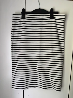 Randig kjol från KappAhl - Säljer en snygg, vit och svart randig kjol från KappAhl. Kjolen har en rak passform och är gjord i mjuk bomull, perfekt för en stilren och enkel look. Passar till många olika outfits och är superenkel att matcha.