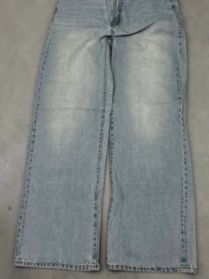 Ljusblåa raka jeans med vintagekänsla - Säljer ett par ljusblå jeans med rak passform och hög midja. Jeansen har en klassisk femficksdesign och slitna detaljer framtill och baktill för en vintage look. Perfekta för en avslappnad och trendig stil. Materialet är denim i bomull.