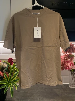 Beige t-shirt från Acne Studios - Snygg beige t-shirt från Acne Studios med klassisk passform och korta ärmar. Tillverkad i mjuk bomull och har en diskret Acne Studios-logga framtill. Perfekt basplagg för en clean och stilren look.