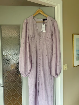 Ljuslila broderad långklänning Gina Tricot - Broderad långklänning från Gina Tricot i ljuslila med vackra blommiga detaljer. Klänningen har långa puffärmar, v-ringad kant och knappar framtill. Perfekt för dig som vill ha en romantisk och trendig look. Aldrig använd och prislapp kvar. Originalpris 699kr