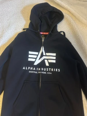 Svart hoodie från Alpha Industries - Svart hoodie med dragkedja från Alpha Industries. Säljer då den är för liten för mig.
