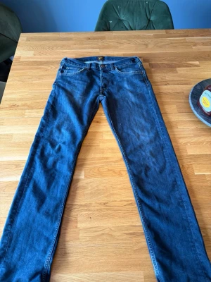 Mörkblå raka jeans från Lee - Snygga mörkblå jeans från Lee med klassisk femficksmodell och raka ben. Jeansen har Lee-lappen bak i midjan och är tillverkade i slitstark denim. Perfekta för dig som gillar en tidlös och enkel stil.det är model Daren med storlek W31 L32