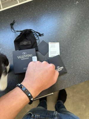 Valentino Garavani svart armband   - Snyggt svart armband från Valentino Garavani med ikoniska pyramidformade nitar i silverfärg. Perfekt nu till sommaren som ger ens outfit lite extra krydda. Nypris 3000kr , armbandet är i inprincip helt nytt allt medföljer även samt äkthetsbevis ! Om ni har några frågor tveka inte att fråga 😊