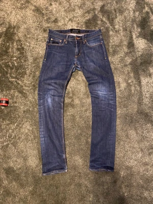 Mörkblå slim fit jeans - Säljer ett par mörkblå slim fit jeans med klassisk femficksdesign och kontrastsömmar. Jeansen har lätt slitna detaljer på låren och knäna för en snygg, avslappnad look. Tillverkade i stretchig denim för extra komfort.