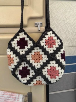Virkad handväska med retro mönster - Unik handväska i virkat material med klassiska rutmönster i svart, vitt, rosa, aprikos. Väskan har en mjuk och bohemisk känsla med lång axelrem och geometriska former. Perfekt för dig som gillar vintage och färg. Virkad av mig i akrylgarn