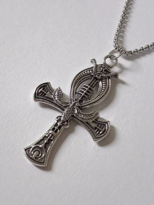Silverfärgat ankh-halsband - Unikt halsband med en stor, detaljerad ankh-symbol i silverfärgad metall. Hänget har egyptiska mönster och en orm samt vingar som dekoration. Kedjan är klassisk och matchar hängets metalliska look. Perfekt för dig som gillar mystiska och historiska smycken. Materialet rostfritt stål. 