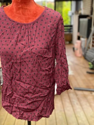 Vinröd prickig blus från b.young 42 - Långärmad prickig topp i viskos Längd: 68 cm Bystvidd: 52 cm Har släppt lite i sömmen runt halsen, se bild 5!  Inga bilder på mig! Katter finns i hemmet!