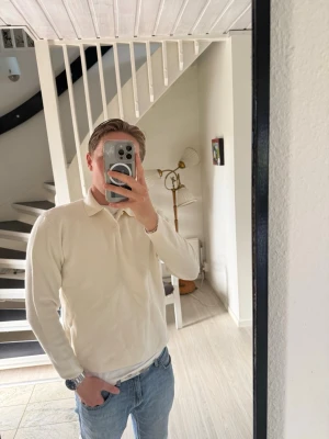 Klassisk vit pikétröja långärmad - Snygg långärmad vit pikétröja med krage och knappar framtill. Tröjan har en clean och stilren look som passar till jeans eller chinos. Perfekt för dig som gillar enkel och tidlös stil. 