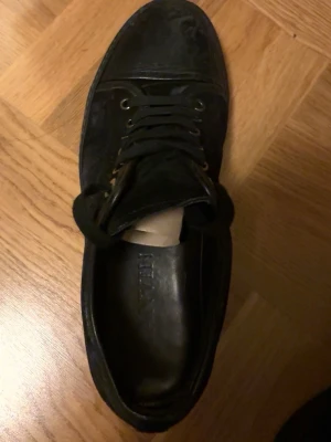  Lanvin - Stilrena svarta sneakers från Lanvin med lågt skaft och klassisk snörning. Skorna har en ovandel i läder och en robust gummisula med Lanvin-logga undertill. Perfekta för dig som gillar minimalistisk och tidlös design.