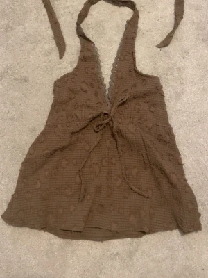 Brun halterneck topp med knyt - Säljer en brun halterneck topp med knyt i nacken och under bysten. Helt ny med prislapp  