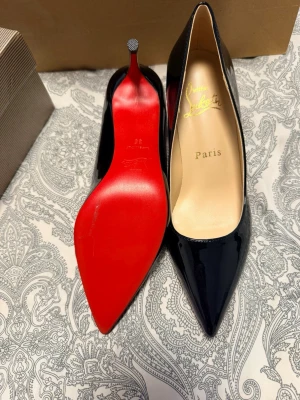 Svarta lackpumps från Christian Louboutin - Snygga svarta pumps i lack från Christian Louboutin med klassisk spetsig tå och hög klack. Skorna har den ikoniska röda sulan och elegant siluett, perfekta för att lyfta vilken outfit som helst.