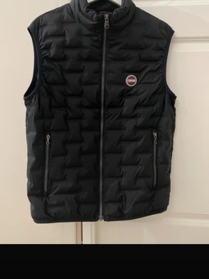 Svart dunväst från Colmar - Snygg svart dunväst från Colmar med quiltat mönster. Västen har två dragkedjefickor framtill och en diskret logotyp på bröstet. Storlek 48. 