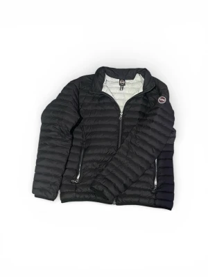 Svart pufferjacka från Colmar - Säljer en svart pufferjacka från Colmar med quiltad design och hög krage. Jackan har dragkedja framtill och två sidofickor med dragkedja. Insidan är ljusgrå och märket sitter på ärmen. Perfekt för dig som vill ha en stilren och varm jacka.