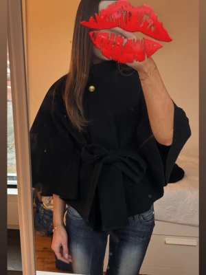 Svart cape-kappa med knytband från Missay  - Stilren svart cape-kappa med knytband i midjan från Missay! Säljer pga att den inte kommer till användning. Kappan är helt utan skråmor och är därför i mycket bra skick💋perfekt att köpa nu inför våren!  