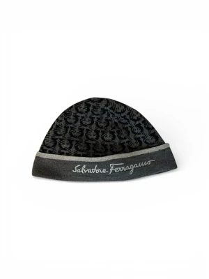 Mörkgrå mönstrad mössa Ferragamo - Snygg mörkgrå mössa från Salvatore Ferragamo med diskret mönster i svart och grått. Mössan har en vikt kant med broderad logotyp framtill och är tillverkad i mjukt stickat material. Perfekt för dig som vill ha en stilren accessoar med lyxig känsla.