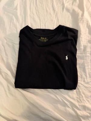 Polo Ralph Lauren T-shirt  - Snygg svart t-shirt från Polo Ralph Lauren med klassisk vit logga broderad på bröstet. Modellen är slim fit och har rund hals. Tillverkad i 100% bomull för en skön och mjuk känsla. Perfekt basplagg till garderoben.