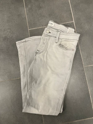 Ljusgrå jeans från Jack&jones - Säljer ett par ljusgrå jeans från jack&jones med klassisk femficksmodell (slim/Glenn)och kontrastsömmar på bakfickan. Jeansen har normal midja, raka ben och är tillverkade i mjukt bomullstyg. Perfekta för en clean och stilren look. Negativit är att läder lappen där bak på jeans har trillat av 