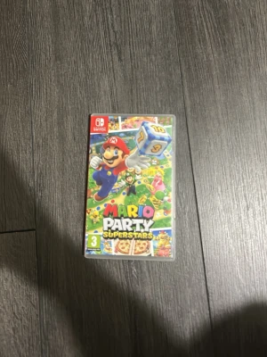 Mario Party Superstars Nintendo Switch - Mario Party Superstars till Nintendo Switch med färgglad plastfodral. Spelet bjuder på klassiska Mario-karaktärer och massor av minispel. Perfekt för spelkvällar med vänner och familj. Omslaget är färgglatt med Mario i fokus och ikoniska spelbräden i bakgrunden.