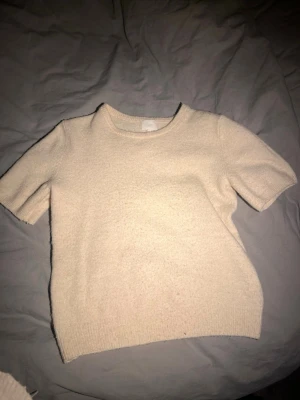 Beige stickad kortärmad tröja H&M - Säljer en beige stickad tröja från H&M med korta ärmar och rund halsringning. Den är lite nopprig men är snygg ändå!💞