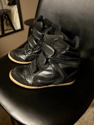 Svarta high top sneakers med kardborre - Snygga svarta high top sneakers med kardborreband och detaljer i både mocka och läder. Skorna har en chunky gummisula i beige och coola paneler som ger en sportig vibe. Perfekta för dig som vill sticka ut med din stil.