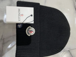 Svart ribbstickad mössa från Moncler - Säljer en svart ribbstickad mössa från Moncler med klassisk Moncler-logga framtill. Mössan är tillverkad i mjukt material och har en uppvikt kant för extra stilpoäng. Perfekt accessoar för kalla dagar och snygg till alla outfits. Priset kan diskuteras 