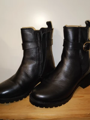 Svarta läderstövletter från Dasia - Snygga svarta stövletter från Dasia i äkta läder. Boots med grov sula, dragkedja på sidan och dekorativt spänne. Klassisk och stilren design som passar till många outfits. Perfekta för dig som vill ha både komfort och edge i din look. Ej använda men har inte kvar originalförpackningen. 