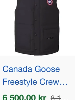 Svart dunväst Canada Goose - Snygg svart dunväst från Canada Goose med klassisk Freestyle Crew-design. Västen har två stora fickor framtill, diskret logga på bröstet och är perfekt för lager-på-lager-stil. Fylld med dun för extra värme och har en stilren, rak passform.