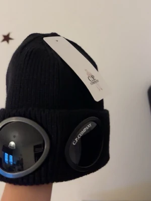C.P. Company mössa - Svart stickad mössa från C.P. Company med de klassiska goggle-linserna framtill. Helt ny.