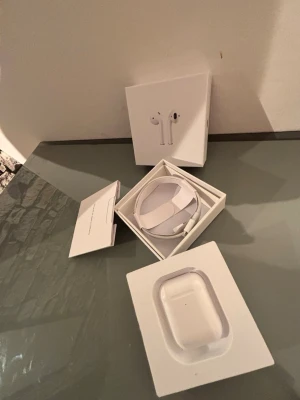 Apple AirPods med laddningsetui - Säljer ett par vita Apple AirPods med laddningsetui och originalförpackning. Trådlösa hörlurar i stilren design, tillverkade i plast. Laddningskabel och manual medföljer. Perfekta för musik, samtal och vardagsbruk.