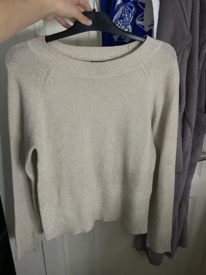 Beige stickad tröja Vero Moda - Mysig beige stickad tröja från Vero Moda med rund halsringning och långa ärmar. Tröjan har ribbade muddar vid ärmslut och nederkant, perfekt för lager på lager. Enkel och stilren design som passar till det mesta. Lite nopprig och har ett litet svart sträck från en penna på armen men inget man tänker på 