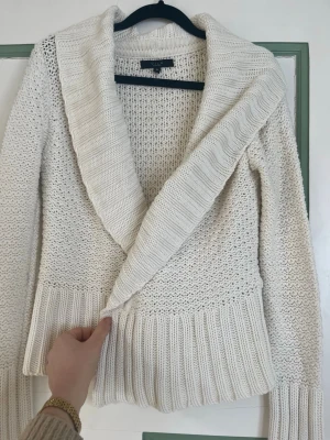 Vit stickad kofta med sjalkrage - Mysig vit stickad kofta från Lindex med bred sjalkrage och knäppning framtill. Koftan har olika stickade strukturer och bred ribbstickning vid ärmslut och nederkant. Perfekt att slänga på sig när det är kyligt ute.