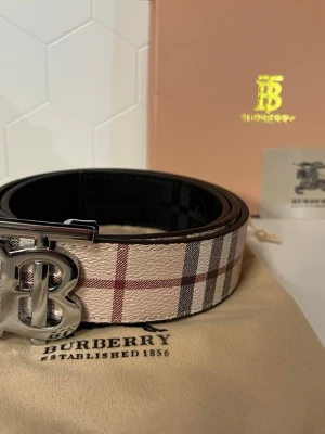 Burberry bälte med klassiskt rutmönster - Storleken är 105, och skärpet skickas samma dag! Snyggt Burberry-bälte med det ikoniska beigea och bruna rutmönstret och en stor silvrig BB-logga som spänne. Perfekt accessoar för att lyfta vilken outfit som helst. Kommer med originalpåse och box. 