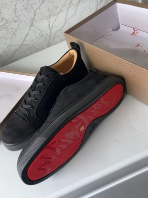 Louboutin skor  - Stilrena svarta sneakers från Christian Louboutin i mocka och läder med klassisk röd sula. Lågt skaft, svarta skosnören och diskret design som sticker ut med den ikoniska röda undersidan. Perfekta för dig som gillar exklusiva detaljer.