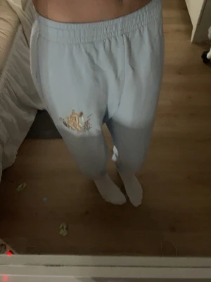 Ljusblå mjukisbyxor med brodyr - Säljer ett par ljusblå mjukisbyxor med broderad detalj av Tiger från Nalle Puh på ena benet. Byxorna har resår i midjan och muddar vid bensluten samt sidofickor. Perfekta för chill dagar hemma eller när du vill ha en avslappnad stil.